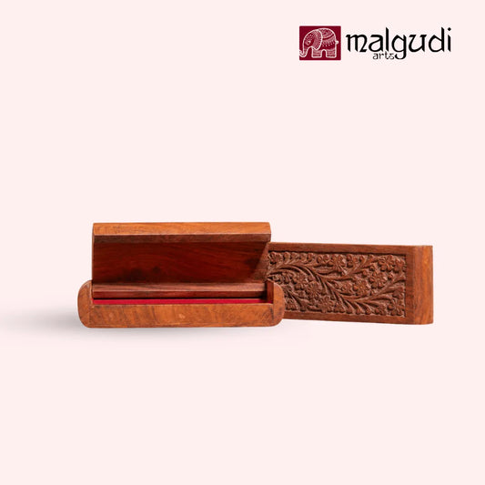A carved wooden box with an open lid and a red interior, shown on a light beige background with the Malgudi Art & Craft logo in the top right corner.